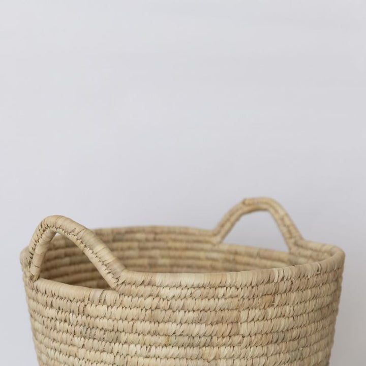 Handwoven palm leaf laundry basket with sturdy handles and natural texture, available in oval or round shape, a versatile and stylish storage solution for any space.