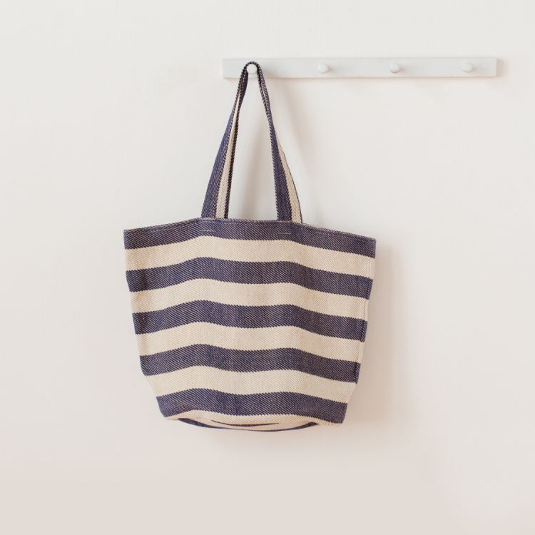 Our striped tote in indigo is handcrafted in sustainable with leather handles, ined with cotton, features an internal zippered pocket and mobile phone pocket for a eco-friendly and sustainable style.