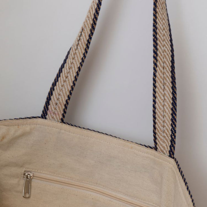Our striped tote in indigo is handcrafted in sustainable with leather handles, ined with cotton, features an internal zippered pocket and mobile phone pocket for a eco-friendly and sustainable style.