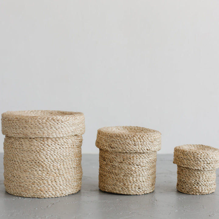 Set of 3 lidded round jute baskets with natural tones and texture compliment an array of design aesthetic. Storage with style in three sizes.